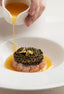 Caviar-topped tartare with sauce being poured.